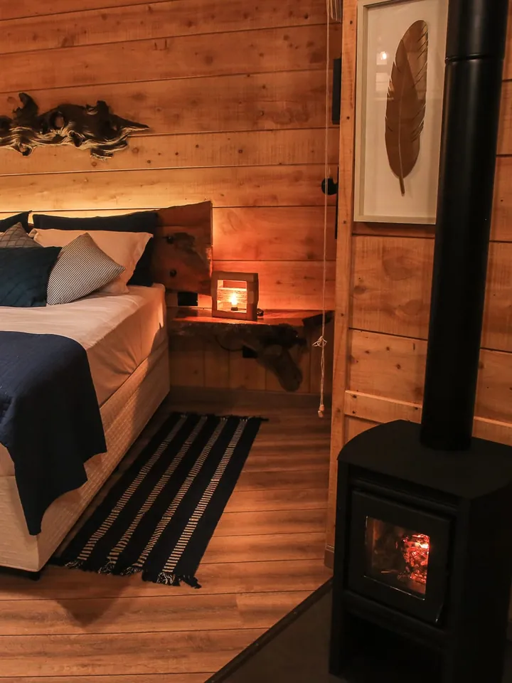 Quarto de madeira da Aconchego com a lareira a lenha ao lado da cama