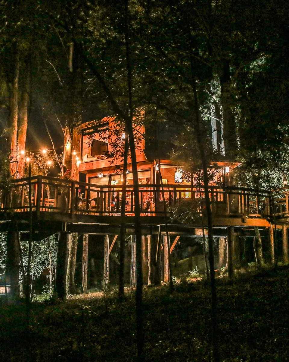 A casa na árvore Aconchego à noite, com o deck iluminado entre as árvores