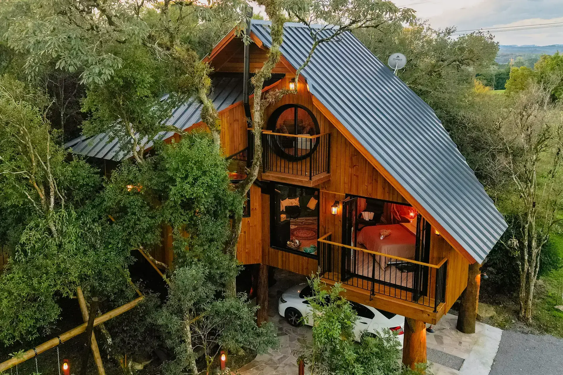 A casa na árvore ao entardecer, com as luzes acesas no meio do bosque